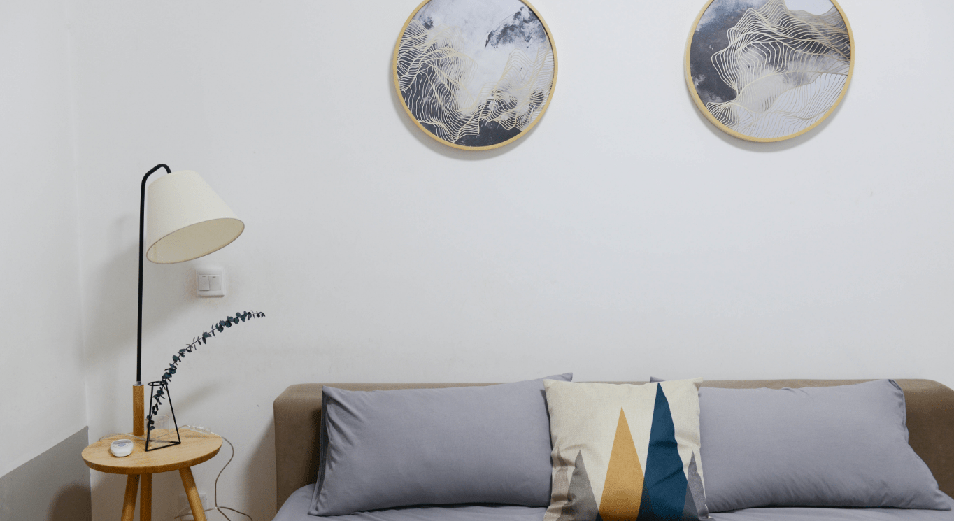 Spazio e organizzazione con il Feng Shui: Divano con cuscini chiari. sulla sinistra una lampada e sulla parete dei quadri tondi.