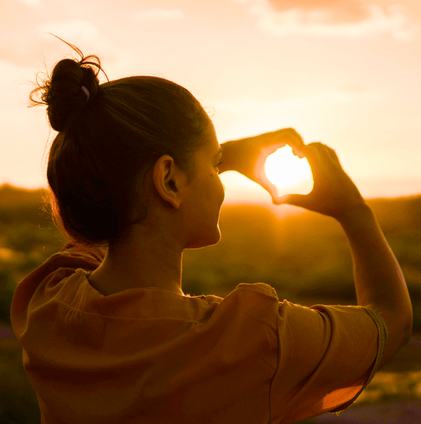 Ragazza crea un cuore con le mani davanti ad un tramonto. Il Ba Zi l'ha portata a fare la cosa giusta lungo il suo percorso di vita