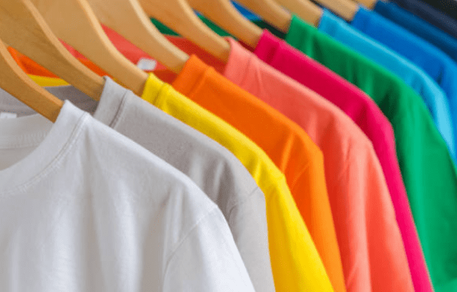 Tante magliette di diverso colore appese a grucce di legno