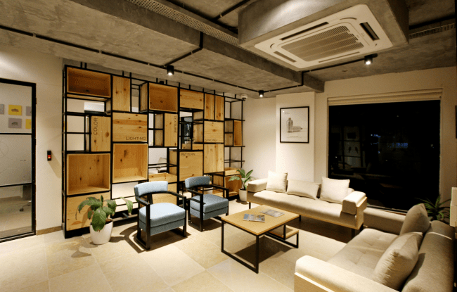 Open space con 2 divanetti color crema e due sedie azzurre. Dietro una struttura in legno e metallo