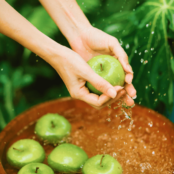 Mani di donna che lavano una mela colta da un cesto di legno