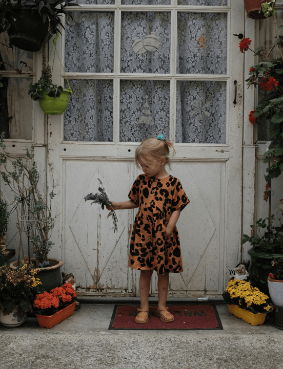 Bambina con un vestitino arancione e nero tiene in mano una pianta davanti alla porta di casa. Le consulenze feng shui di Raffaela Marescalco ti cambieranno la vita