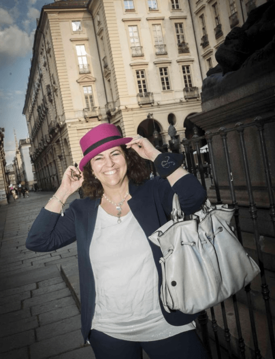Raffaela Marescalco sfoggia un sorriso mentre posa in centro a Torino. Indossa giacca e pantaloni blu, una maglietta bianca e un cappello color fucsia mentre porta la sua borsa color perla.
