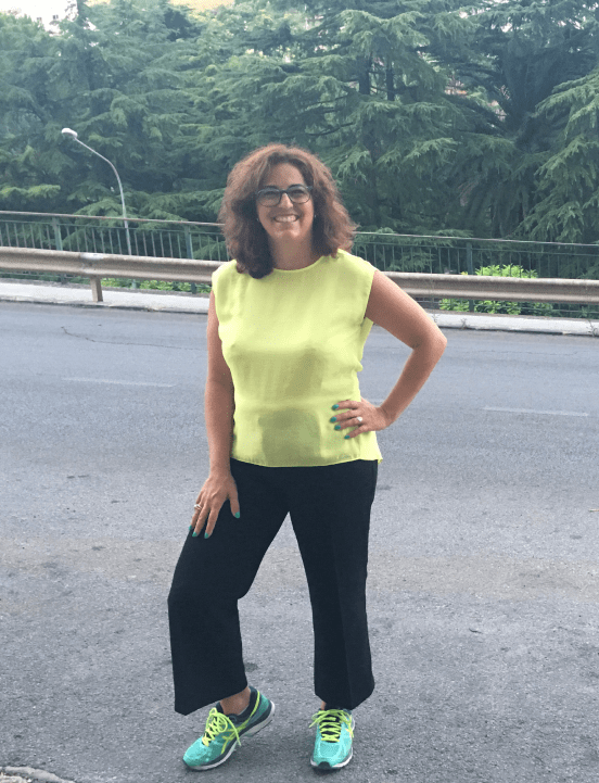 Raffaela Marescalco posa in tenuta da corsa. Indossa una maglia smanicata gialla, pantaloni lunghi neri e scarpe da corsa color verde acqua.