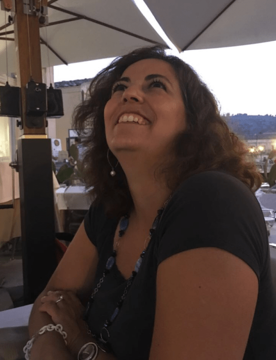 Raffaela Marescalco seduta all'aperto sotto un ombrellone, che guarda verso l'alto.